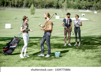 Young And Elegant Friends Standing Together With Golf Equipment, Having Fun During A Golf Play On The Beautiful Course On A Sunny Day