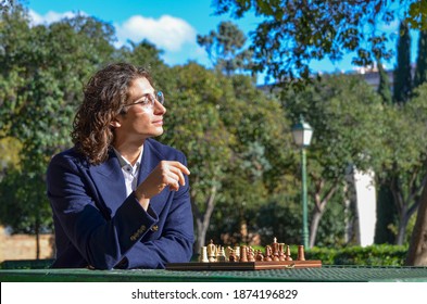 Young Elegant Guy Playing Chess in Park Table with the Wind Moving his Hair - Powered by Shutterstock