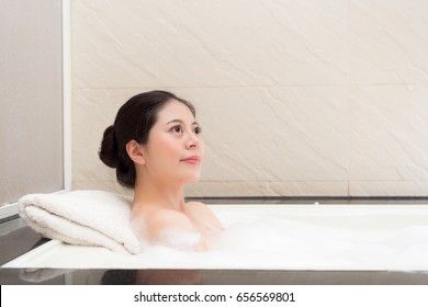 young elegant lady lying down in bathtub and looking at air thinking daydreaming enjoying bathing time with bubble water.