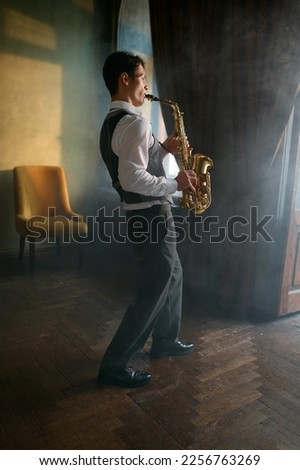 Young elegant man playing gold alto saxophone in misty room
