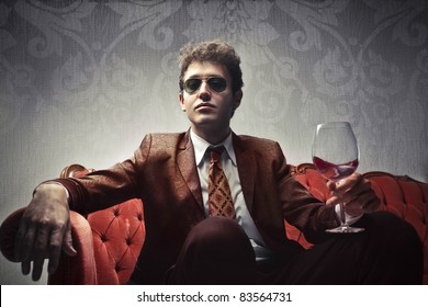 Young elegant man sitting on a velvet sofa and holding a glass of wine