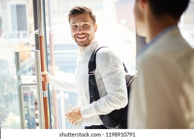 Young Elegant Man With Trendy Backpack Walking Out Of Cafe Door And Smiling Over Back Saying Goodbye