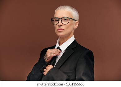 Young Elegant Masculine Female In Black Jacket, White Shirt And Eyeglasses Touching Necktie While Getting Dressed For Work Or Formal Event