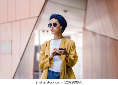A young, elegant and stylish Middle Eastern listens to music on hear wireless earphones that is streaming from her smartphone. She is wearing a turban (hijab, head scarf) and is dancing.