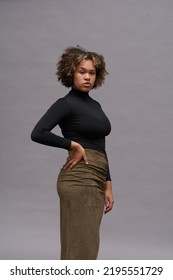 Young elegant woman in classy black turtleneck and long khaki skirt posing over grey background in isolation in front of camera