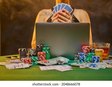 Young elegant woman plays poker in an online casino. On a green gambling table, a laptop, cards, chips. Brown smoky background. Online casino, gambling, poker, risk, chance of luck, gambling addiction