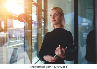 Young elegant woman thinking something while standing with touch pad near office window outside, female employer holding digital tablet while looking forward to meeting with international partners - Shutterstock ID 379992868