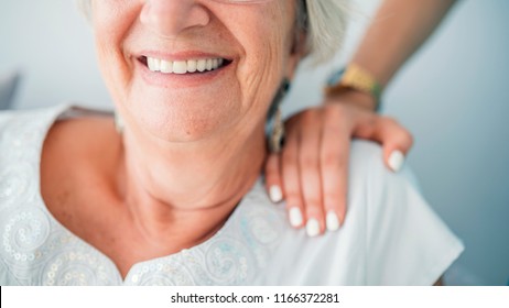 Young elegant woman's hand on senior lady's shoulder. Portrait of a smiling old lady with her nurse's hands on her shoulders. Sign of caring for seniors. Helping hands. Care for the elderly concept.  - Powered by Shutterstock