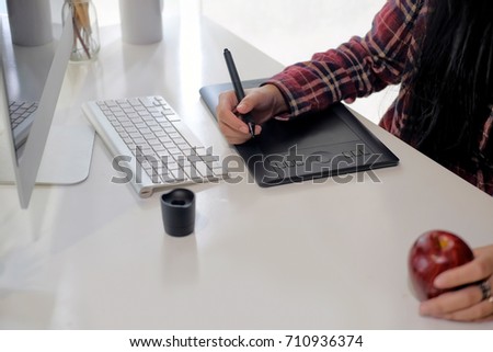 Young emale designer using graphics tablet while working with computer at studio or office.