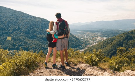 Young, embraced couple enjoying the fantastic mountain and valley panorama, taking a break on a viewpoint after a hike on a sunny summer day - Powered by Shutterstock