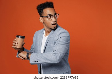 Young employee business man corporate lawyer wear classic formal grey suit shirt glasses work in office use smart watch check time hold cup of coffee run isolated on plain red orange background studio