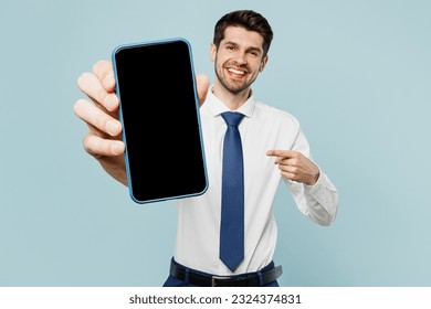 Young employee business man corporate lawyer wear classic formal shirt tie work in office hold use show blank screen workspace area mobile cell phone isolated on plain blue background studio portrait - Shutterstock ID 2324374831