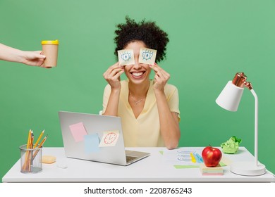 Young Employee Business Woman Of African American Ethnicity Wear Shirt Sit Work At White Office Desk Pc Laptop Pretend Work Hold Sticker Pattern Open Eyes Cup Coffee Isolated On Plain Green Background