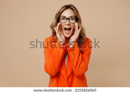 Young employee business woman corporate lawyer wear classic formal orange suit glasses work in office scream sharing hot news about discount with hands near mouth isolated on plain beige background
