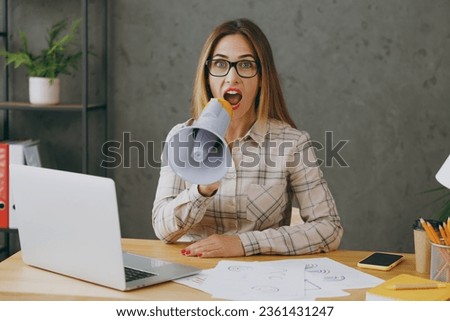 Young employee business woman wear shirt casual clothes glasses sit work at office desk with pc laptop hold in hand megaphone scream announces discounts sale Hurry up. Achievement career job concept