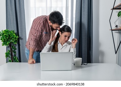 Young Employee Is Harassing His Colleague At Work While She Is Doing Her Job On The Laptop. Young Man Flirting With Woman In The Office.