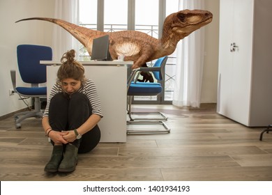 A Young Employee Hides From A Velociraptor In The Office Where She Works. Mobbing Concept Or Surreal Image