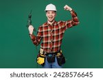 Young employee laborer handyman man wearing red shirt hardhat hat use hold electric drill isolated on plain green background. Instruments accessories for renovation apartment room. Repair home concept