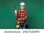 Young employee laborer handyman man wears red shirt hardhat hat use hold electric drill isolated on plain green background. Instruments accessories for renovation apartment room. Repair home concept