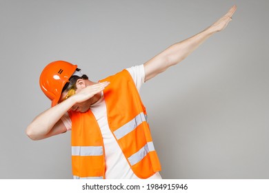 Young Employee Smiling Man In Orange Vest Protective Helmet Hardhat Do Dab Hip Hop Dance Hands Move Gesture Isolated On Grey Background Studio Instruments For Renovation Apartment Repair Home Concept.