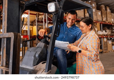 Young employees work in the warehouse. A smiling man and a woman in casual clothes mark the availability of goods on the shelves. The forklift driver and the manager check the documentation and goods - Powered by Shutterstock