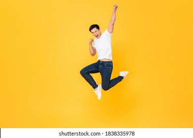 Young energetic Asian man  jumping and raising his fist isolated on yellow color background