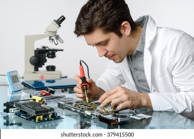 Young energetic male tech or engineer repairs electronic equipment in research facility. Shallow DOF, focus on the face and hands of the worker. - Powered by Shutterstock