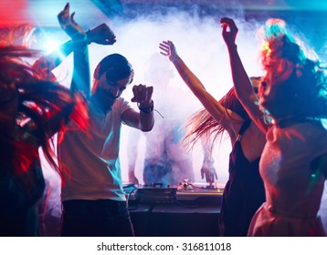 Young energetic people dancing by turntables of dj
