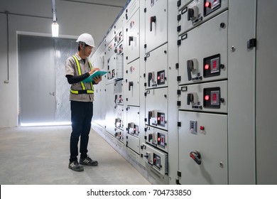Young engineer checking status controller and multi meter of switchgear MDB distribution electrical energy substation at electical room for the industrial factory