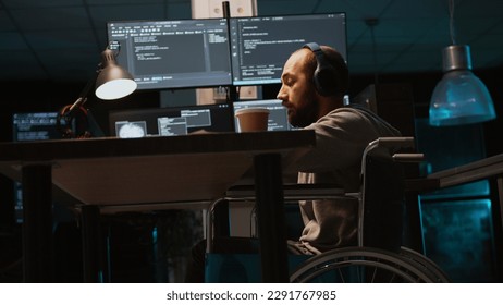 Young engineer with chronic disability working on IT software coding, using source code and data. Male coder wheelchair user with impairment developing system interface. Handheld shot.