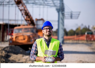 Young engineer controlling drone above building site with metal construction and crane in background