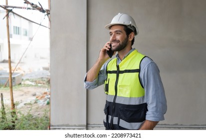 Young Engineer In Hardhat And Safety Vest Talking On Mobile Phone. Work Environment Of Engineers At The Construction Site.