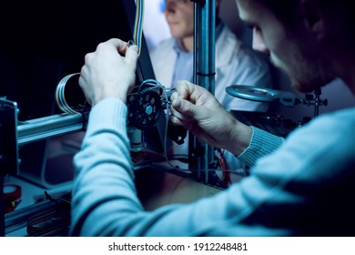 Young Engineer In The Lab Working On A 3D Printer, Another Student Is Working With A Computer On Background, Innovation And Engineering Concept