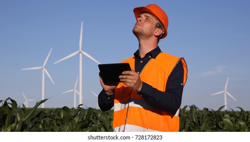 Young Engineer Man Using Digital Tablet Looking Up at Wind Turbines Observing Tower