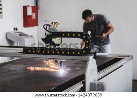 Young engineer setup plasma cutter for work in metalwork workshop.