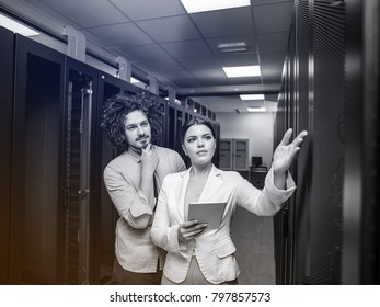 Young IT engineer showing working data center server room to female chief engineer who holding tablet computer
