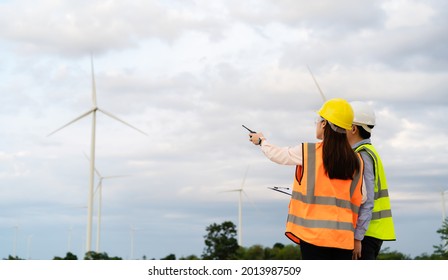 Young Engineer Team Working With Report In Clipboard Against Wind Turbine Farm