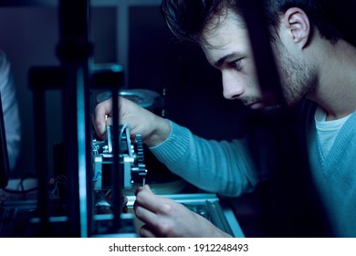 Young Engineer Working At Night In The Lab, He Is Adjusting A 3D Printer's Components, Technology And Engineering Concept