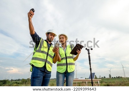 Young engineers team use an anemometer to measure wind speed, temperature and humidity on a wind farm background