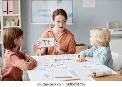 Young English teacher showing the card with letter to children and they learning it at the table during a lesson