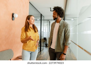 Young enthusiastic female colleague explains new strategy to male employee and gesturing. Indoor portrait of diverse work team discussing, walking through hallway in modern coworking office space - Powered by Shutterstock