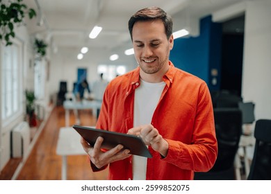 Young entrepreneur smiling while using a digital tablet in a bright, modern office, with colleagues collaborating in the background, highlighting productivity and connectivity