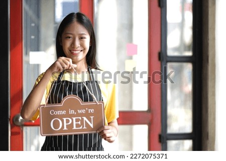 Young entrepreneurial small business holding a store opening sign.