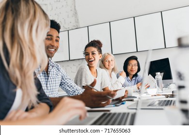 Young Entrepreneurs Discussing Something With Smile During Conference. Indoor Portrait Of International Employees Sitting In Office With Laptops And Talking About Work.