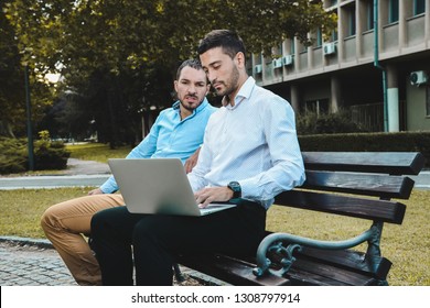 Young entrepreneurs sitting down on a bench in the city. Young businessmen talking and working out a plan. Brainstorming outside on a beautiful day.