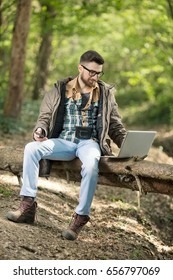 Young Environmentalist Is Doing A Research And Working On A Laptop While Sitting On A Tree Trunk In A Forest