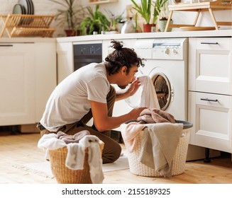 Young Ethnic Black Man Householder With Curly Hair Sitting On Floor Near  Washing Machine While Doing Laundry In Kitchen At Home