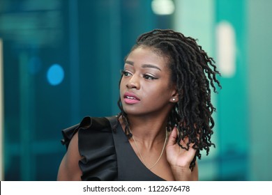 Young ethnic woman in black outfit touching modern hairstyle with dreadlocks and looking away sensually