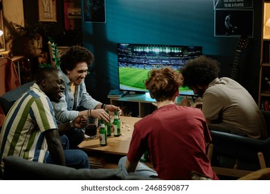 Young ethnically diverse friends enjoying spending evening together watching soccer game, drinking beer and chatting - Powered by Shutterstock