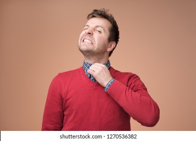 Young europeam man in red sweater feeeling uncomfortable. Colar is tight and stuffy and he tries to expand the collar to make a breath. Hate office clothes